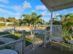 A covered outdoor area with a white bench, a small table, and a railing. - Sun-Soaked Delray Beach 2-Bed, 2-Bath Beauty with Sunroom & Pool Access. (Delray Beach)