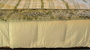Ein Bett mit weißer gesteppter Daunendecke, einem blumigen Überwurf und einem Kopfteil aus Holz.