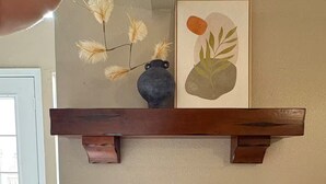 Ein Kamin mit Sims, einem gerahmten Kunstwerk und einer Vase mit Trockenblumen.
