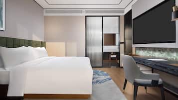 A hotel room with a bed, a desk, a chair, a flat-screen TV, and a minibar.