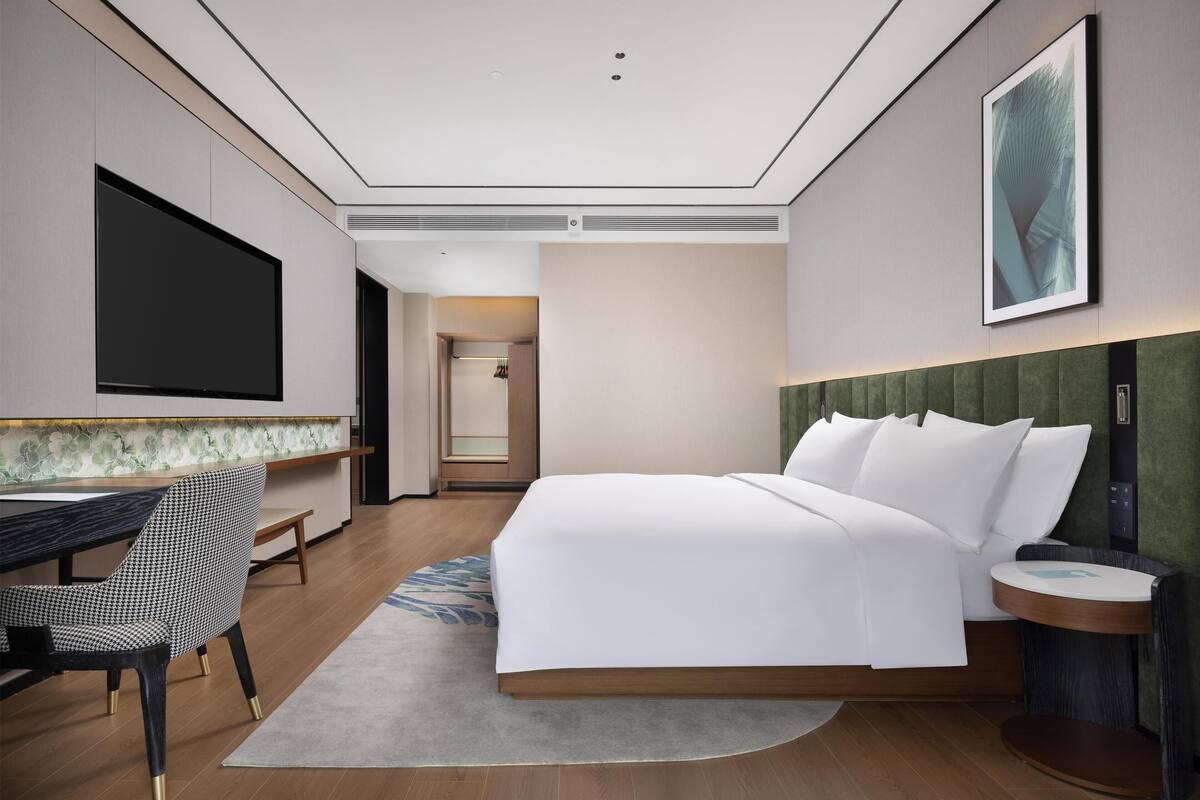 A modern hotel room with a large bed, a desk, a chair, and a television.