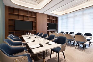 Une salle de conférence équipée d’une longue table, de chaises, d’un grand écran et d’un tableau blanc.