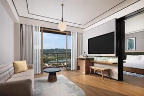 A modern hotel room with a large TV, a sofa, a dining table, and a balcony with a view. - Hilton Garden Inn Chongqing Bishan (Chongqing)