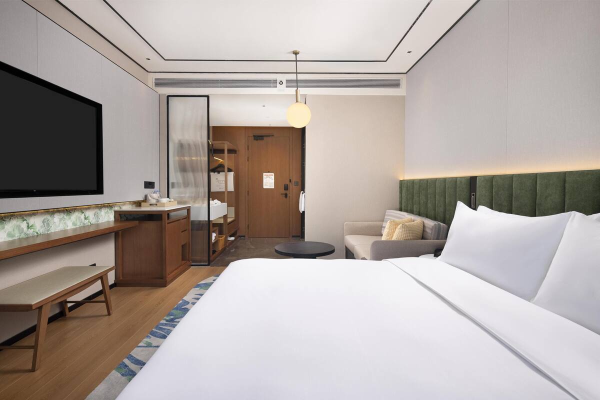 A hotel room with a bed, a desk, a chair, a TV, and a wardrobe.