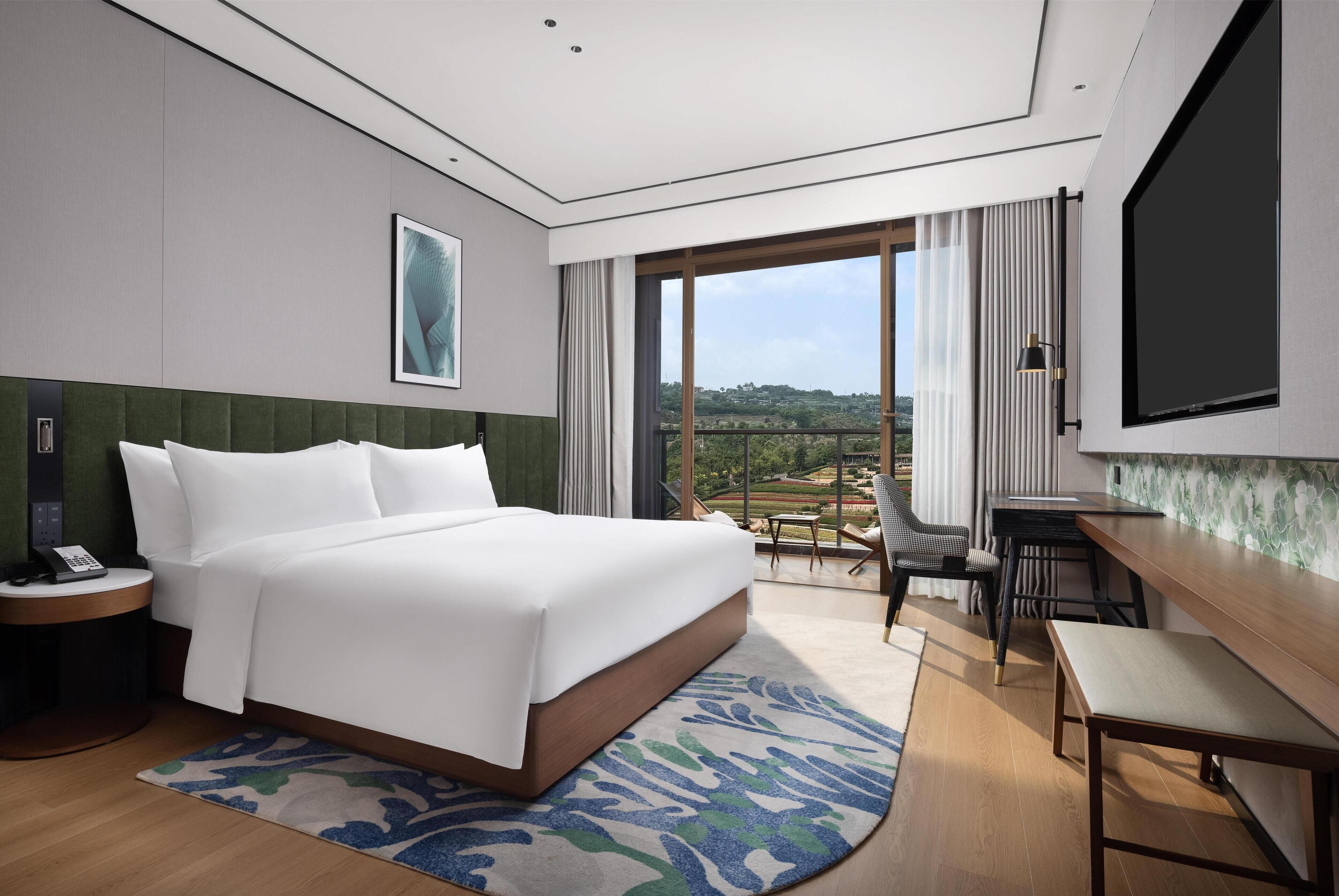Une chambre d’hôtel avec un grand lit, un bureau, une chaise, une télévision et une vue sur l’extérieur.