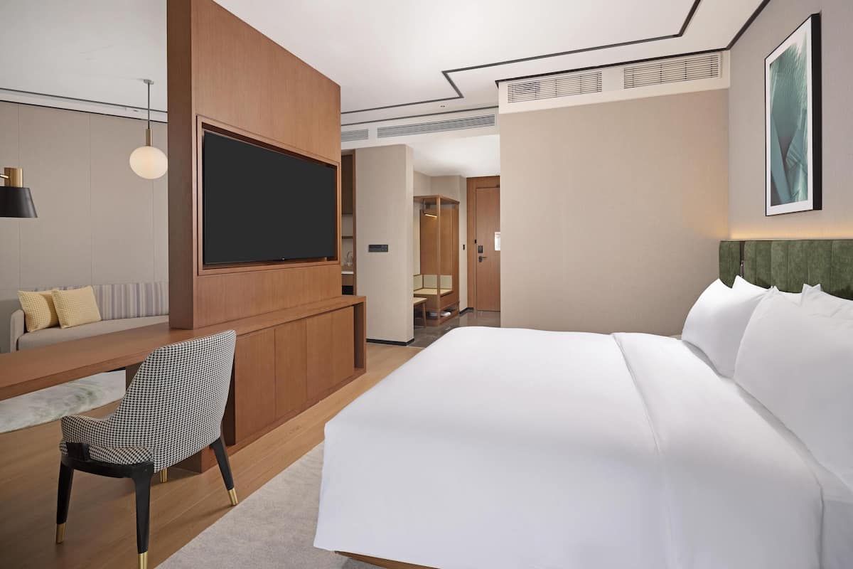 A hotel room with a bed, a desk with a chair, a television, and a wardrobe.
