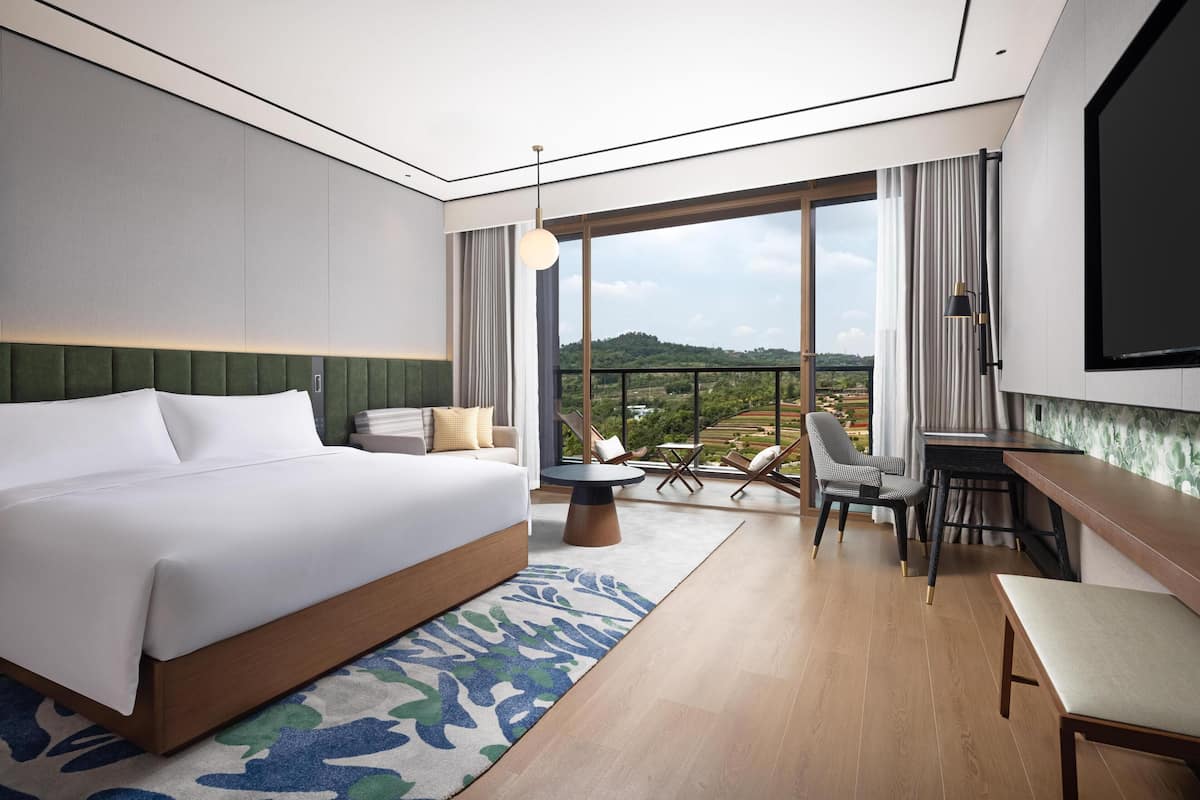 A modern hotel room with a large bed, a dining area, and a balcony with a view.