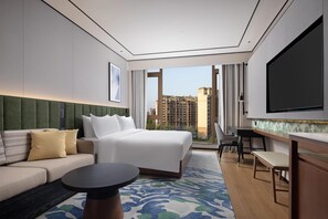 A hotel room with a bed, sofa, desk, and a large TV. - Hilton Garden Inn Chongqing Bishan (Chongqing)