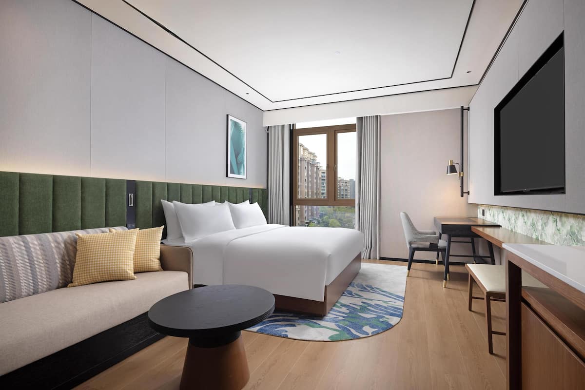 A hotel room with a bed, a sofa, a dining table, a TV, and a window with curtains.