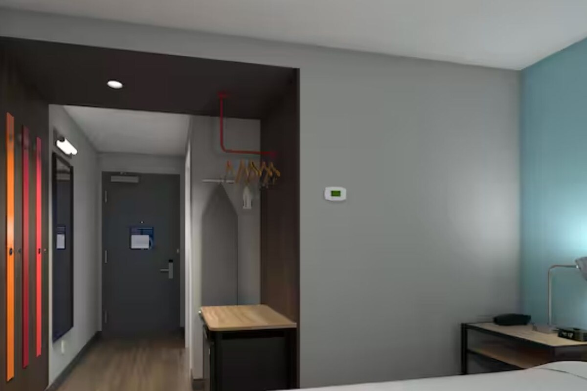 A modern hotel room with a bed, a desk, and a wardrobe.