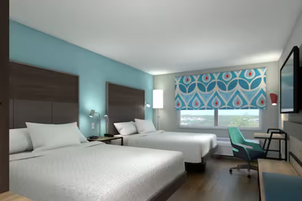 A hotel room with two beds, a desk, a chair, a TV, and a window with a view.