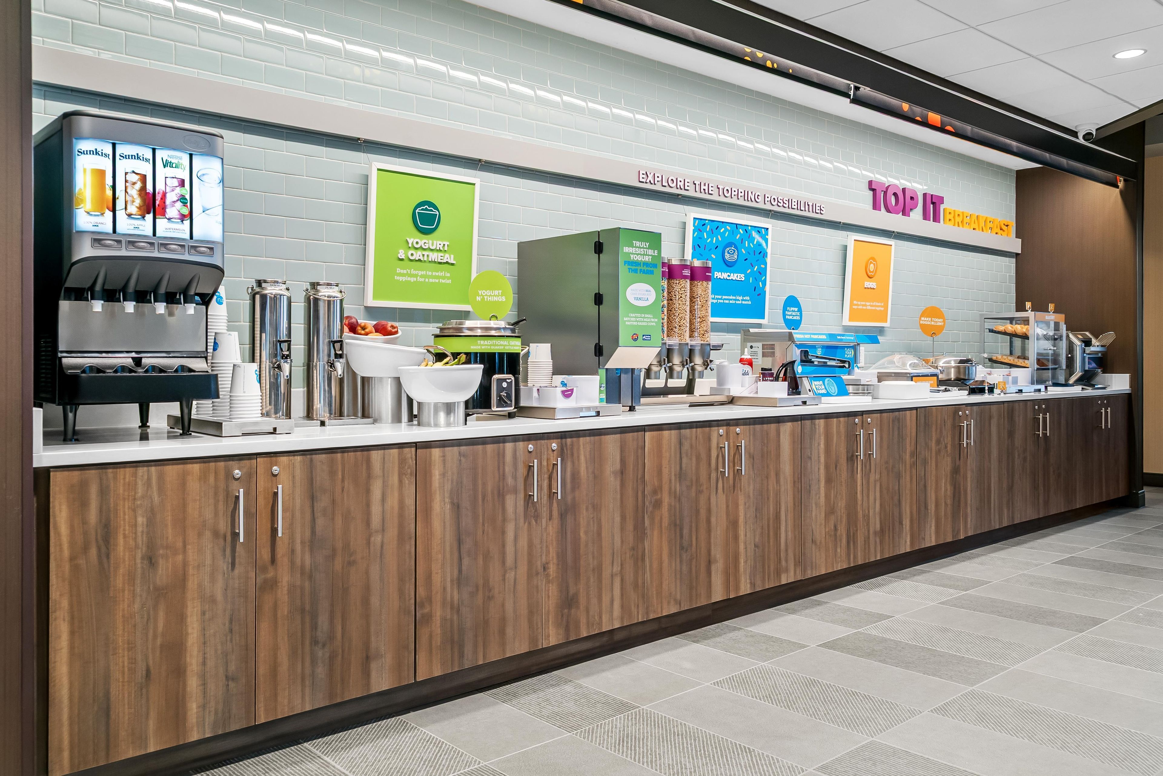 A breakfast bar with a variety of food and drink options, including yogurt, oatmeal, pancakes, and eggs.