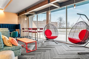 A modern interior with seating arrangements, a hanging chair, and large windows. - Tru By Hilton Hagerstown (Hagerstown)