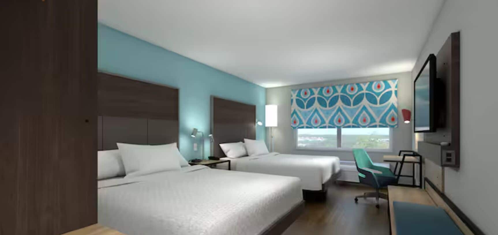 Une chambre d’hôtel avec deux lits, un bureau, une chaise, une télévision et une fenêtre donnant sur un beau paysage.