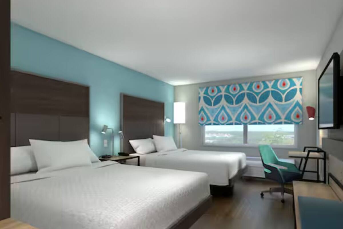 Une chambre d’hôtel avec deux lits, un bureau, une chaise, une télévision et une fenêtre donnant sur un beau paysage.