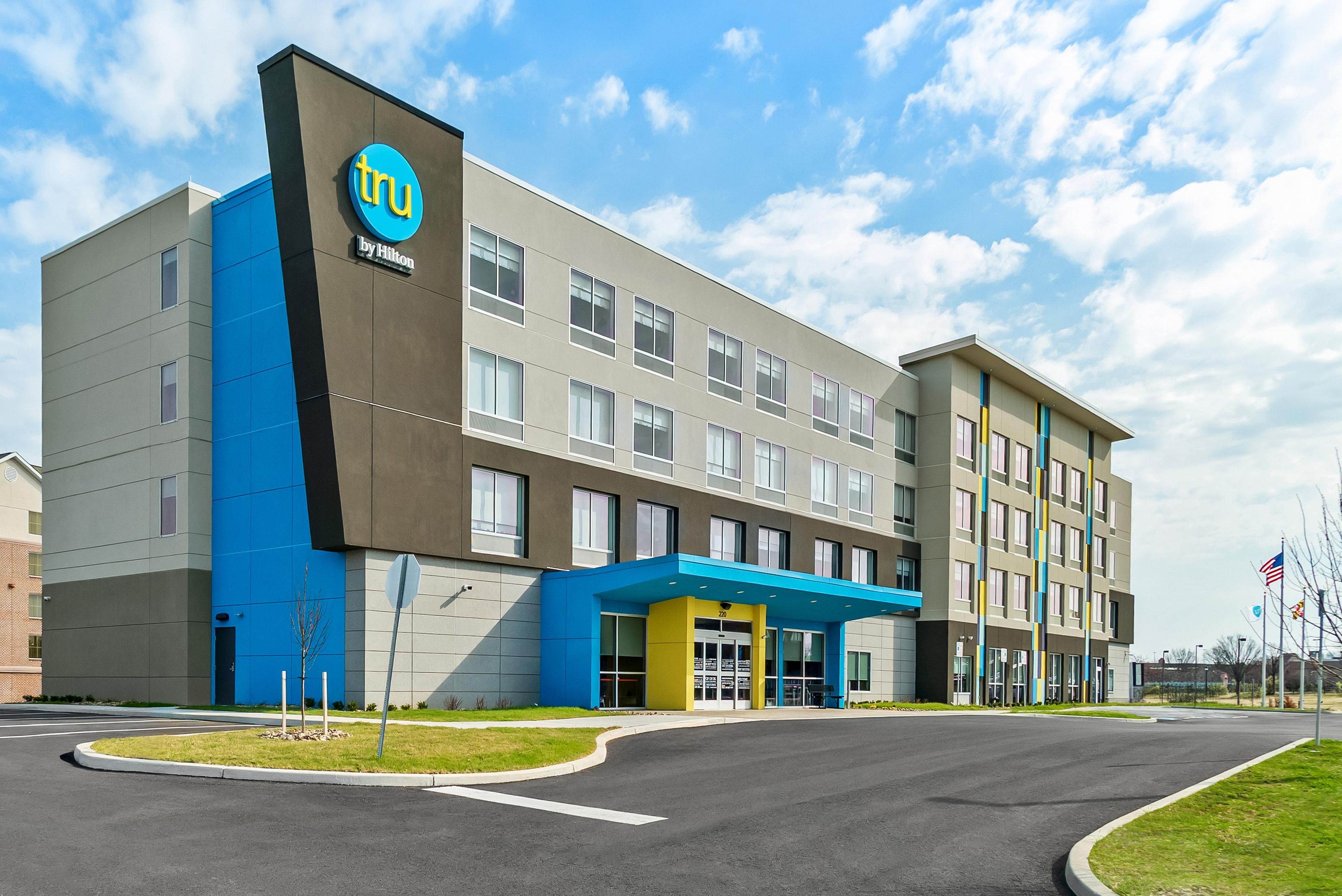 A modern hotel building with a prominent blue logo, a flat roof, and a series of windows.