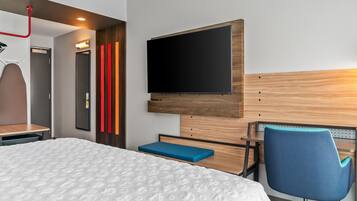 A hotel room with a bed, a desk, a chair, a television, and a mirror.