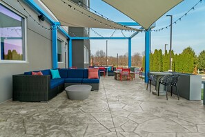 An outdoor patio area with a blue and gray color scheme, featuring a sofa, chairs, a table, and string lights. - Tru By Hilton Hagerstown (Hagerstown)