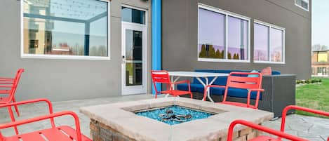 An outdoor patio area with a fire pit, red chairs, and a seating arrangement.