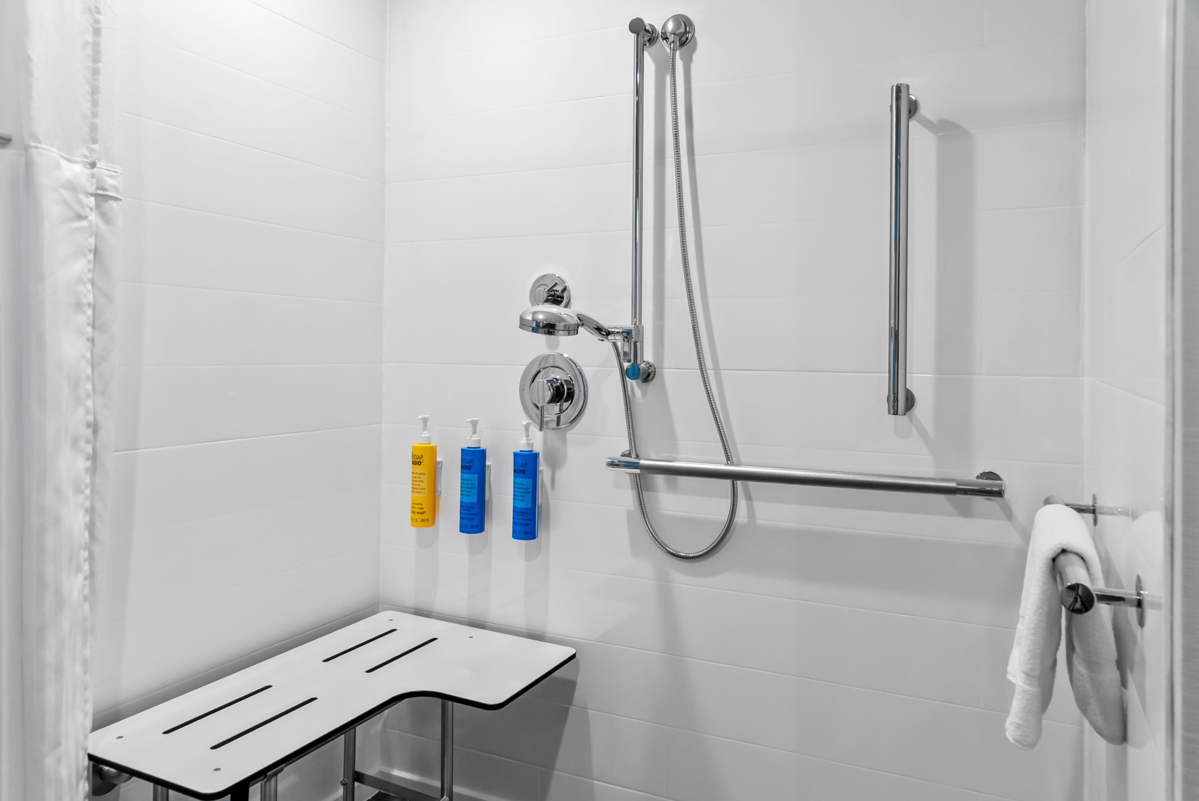 Een moderne douche met een handdouche en een wandmengkraan, een handdoekhouder met een witte handdoek, en drie zeepdispensers op de muur.