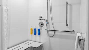 Een moderne douche met een handdouche en een wandmengkraan, een handdoekhouder met een witte handdoek, en drie zeepdispensers op de muur.