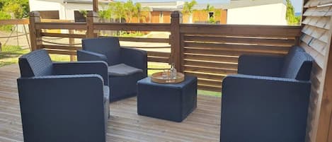 Terraza de madera con mobiliario de mimbre oscuro y una bandeja con botellas.