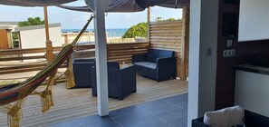 Een overdekt terras met een hangmat, comfortabele stoelen en uitzicht op zee.