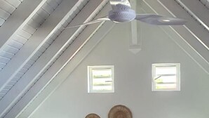 Une chambre avec un plafond en pente, un lit doté d’une tête de lit en bois, deux lampes de chevet et un ventilateur de plafond.