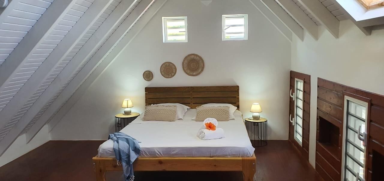 A bedroom with a sloped ceiling, a wooden bed, two bedside tables with lamps, and a small window.