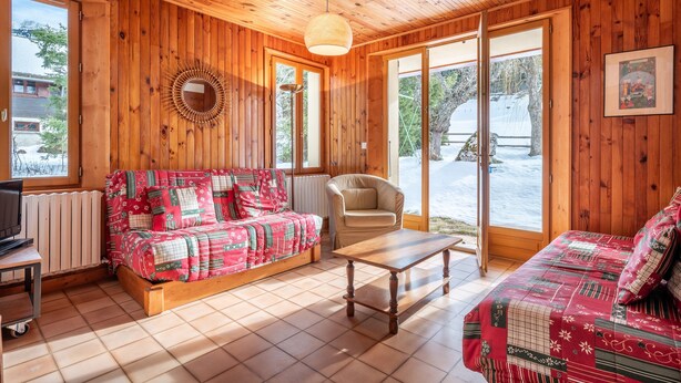 A wooden cabin interior with a sofa, armchair, and a table.