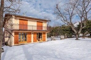 Une maison à deux étages avec des volets en bois, un balcon et une cour enneigée.