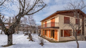 A two-story house with a balcony, surrounded by snow-covered ground and leafless trees.