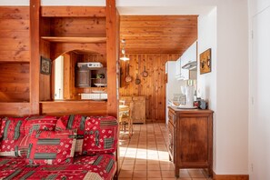L’intérieur chaleureux d’un chalet avec un plafond en bois, un canapé agrémenté de coussins à motifs, un coin cuisine doté de meubles en bois et une table à manger.