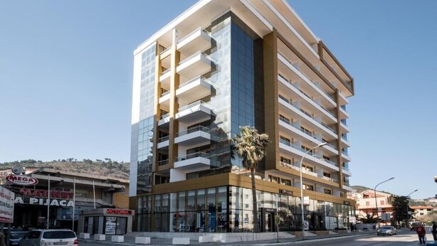 Un hôtel à plusieurs étages doté de balcons, d’une façade en verre et d’un espace commercial au rez-de-chaussée comprenant des boutiques.