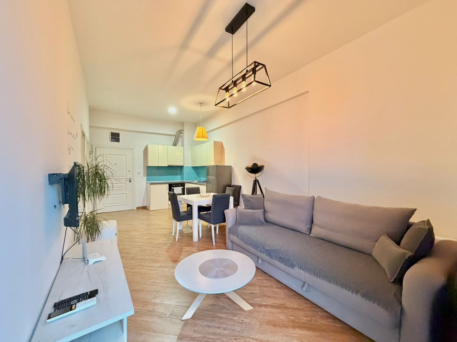 A modern living room with a grey sofa, a round coffee table, and a dining area with a white table and chairs.