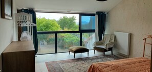 A bedroom with a large window, a bed, a chair, a radiator, and a wooden table. - A beautifully restored Perigordian barn with a large swimming pool (Saint-Paul-Lizonne)