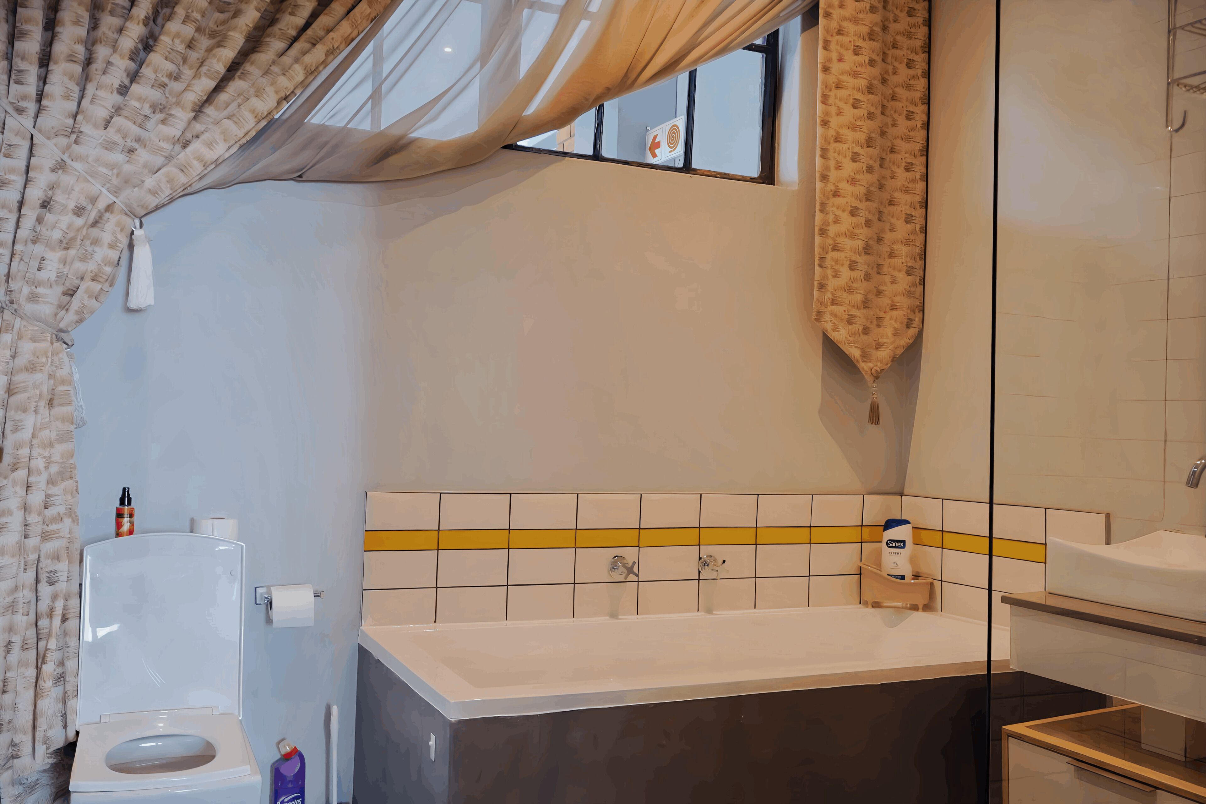 A bathroom with a bathtub, toilet, and a window with curtains.