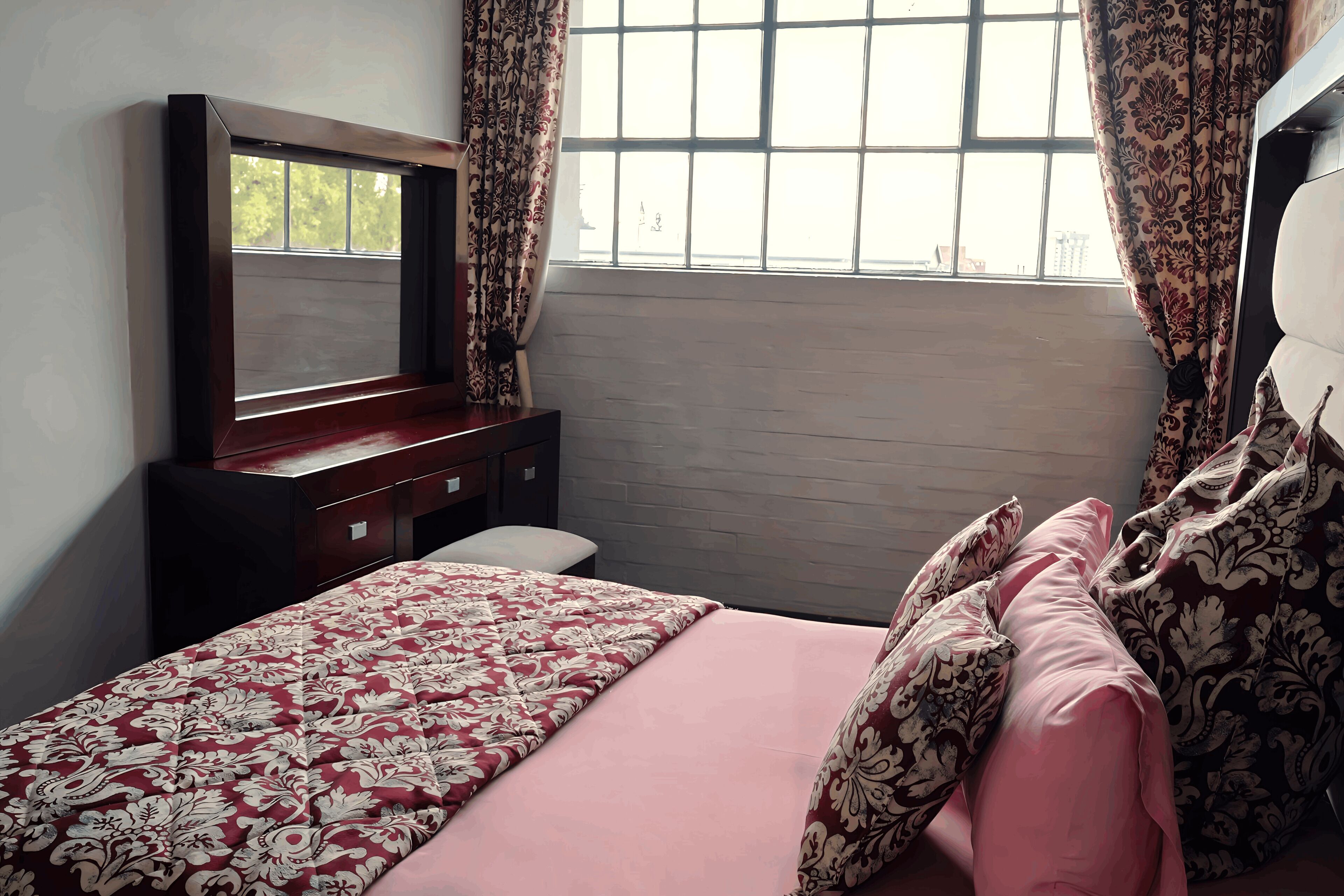 Un dormitorio con cama, cómoda, espejo y ventana con cortinas.