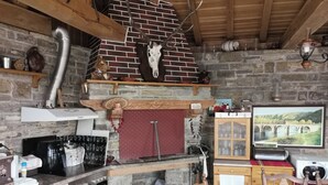 A rustic kitchen with a brick fireplace, a wooden ceiling, and a stone wall.