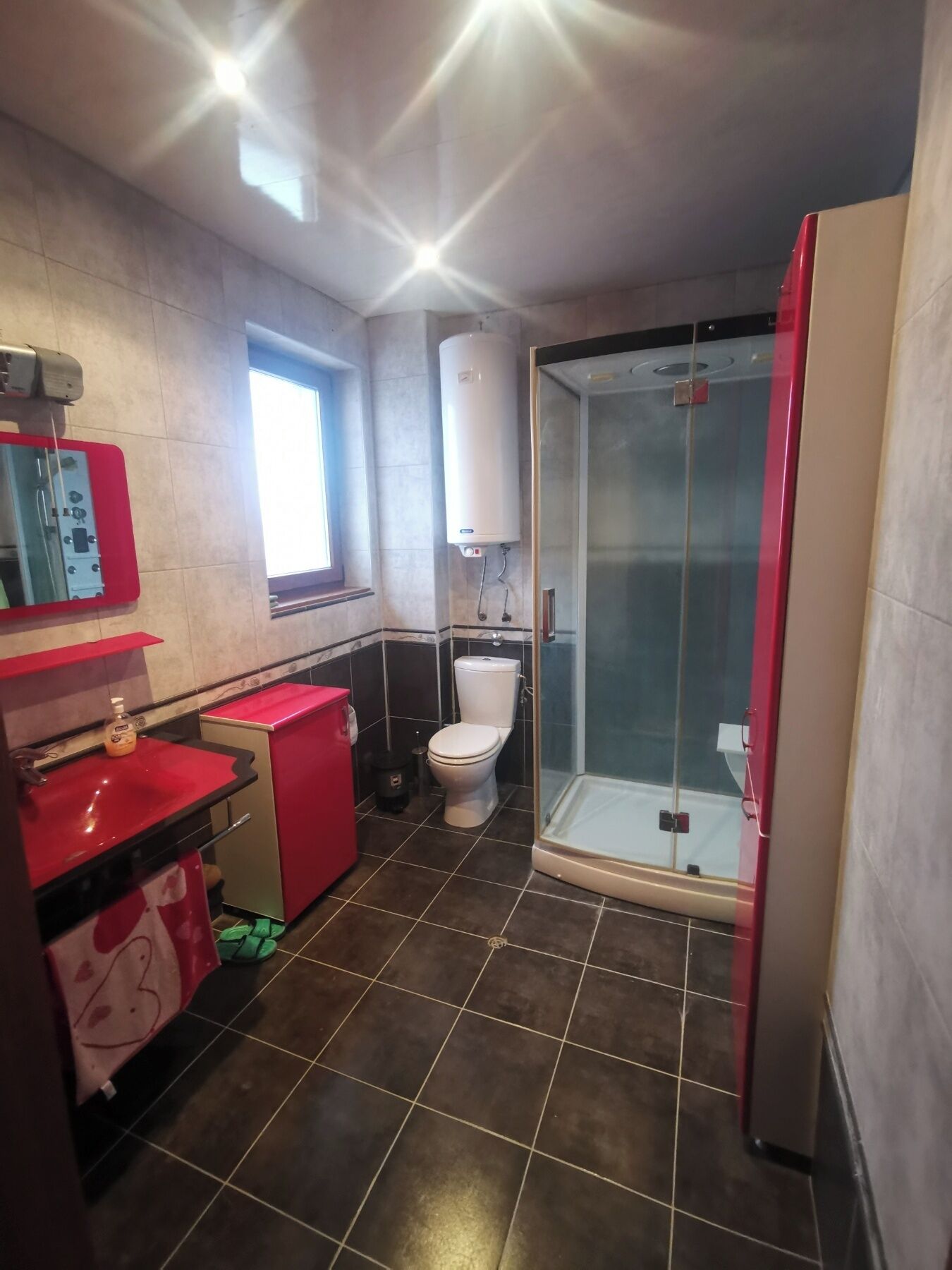 Een badkamer met toilet, douche, rode wastafel en spiegel.