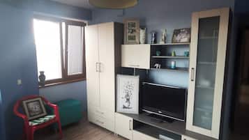 Ein Wohnzimmer mit Holzboden, blauer Wand, einem TV-Schrank mit Flachbildfernseher, einem roten Sessel und einem Deckenventilator.
