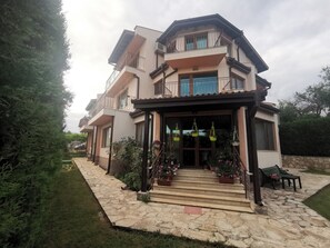 Una casa de dos pisos con entrada empedrada de piedra, plantas en macetas y un banco.