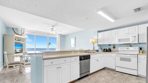 A modern kitchen with white cabinets, a dishwasher, an oven, and a microwave. There is a window with a view of the beach. - Majestic Beach Towers 1-1314 (Panama City Beach)