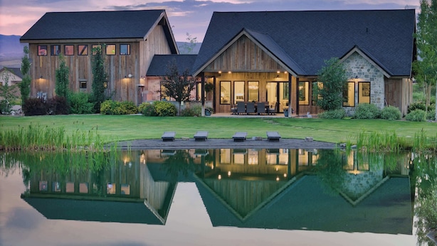 Ein großzügiges, modernes Haus mit einer Fassade aus Stein und Holz, einem gepflegten Rasen und einem Teich, der das Licht reflektiert.
