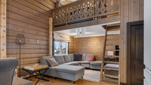 A log cabin interior with a sectional sofa, a dining table, and a ladder leading to a loft area.