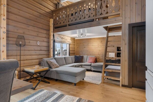 A log cabin interior with a sectional sofa, a dining table, and a ladder leading to a loft area.
