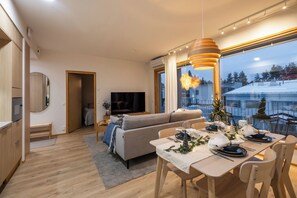 Ein modernes Wohnzimmer mit einer Couch, einem Esstisch für zwei Personen und einem Fernseher im Hintergrund.