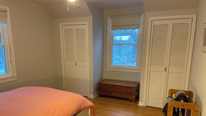 A bedroom with a bed, wooden floor, white closets, a window with a view, and a bench.