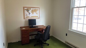 A room with a wooden desk, a black office chair, a computer, and a world map on the wall.