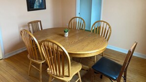 A dining area with a round wooden table surrounded by six wooden chairs, a small potted plant on the table, and a framed artwork on the wall.